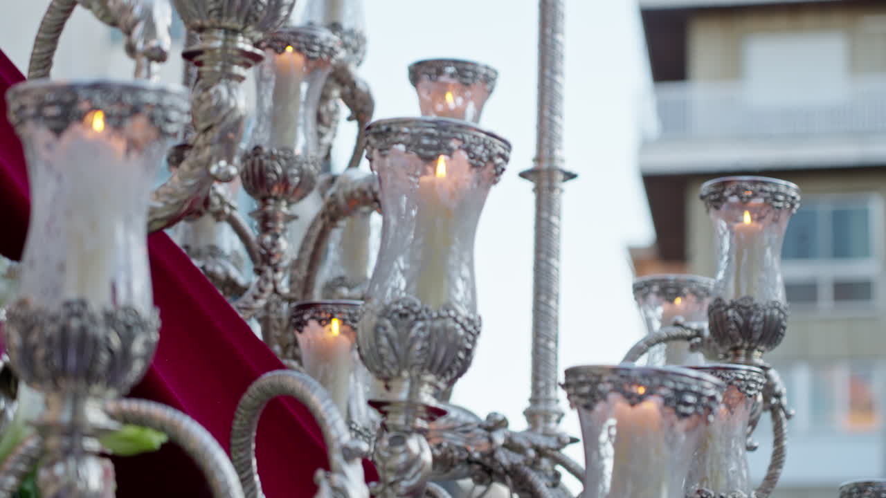 Udsmykket sølvkandelaber oplyst af tændte stearinlys, del af en traditionel religiøs procession i Spanien, der symboliserer tro og hengivenhed