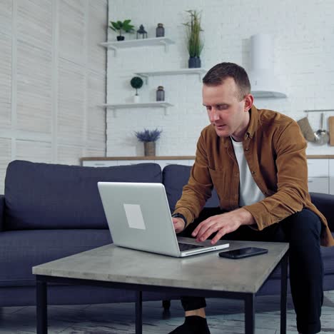 young male working from home. portrait of freelancer man working on laptop at home sitting on couch. quarantine remote work