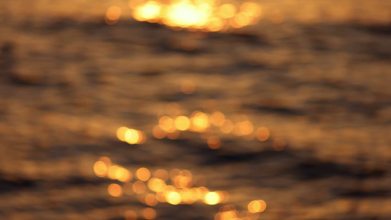 disparo abstracto borroso de la ola del mar al atardecer. círculos de bokeh dorados brillan en las olas. atardecer en el mar, atmósfera romántica y acogedora. cámara lenta, 4k