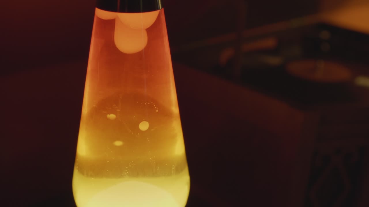 Close up of a vintage lava lamp in a warm and vintage setting with a record player. Orange lighting and bubbles create a retro atmosphere. Shot in 60 Frames for slow motion