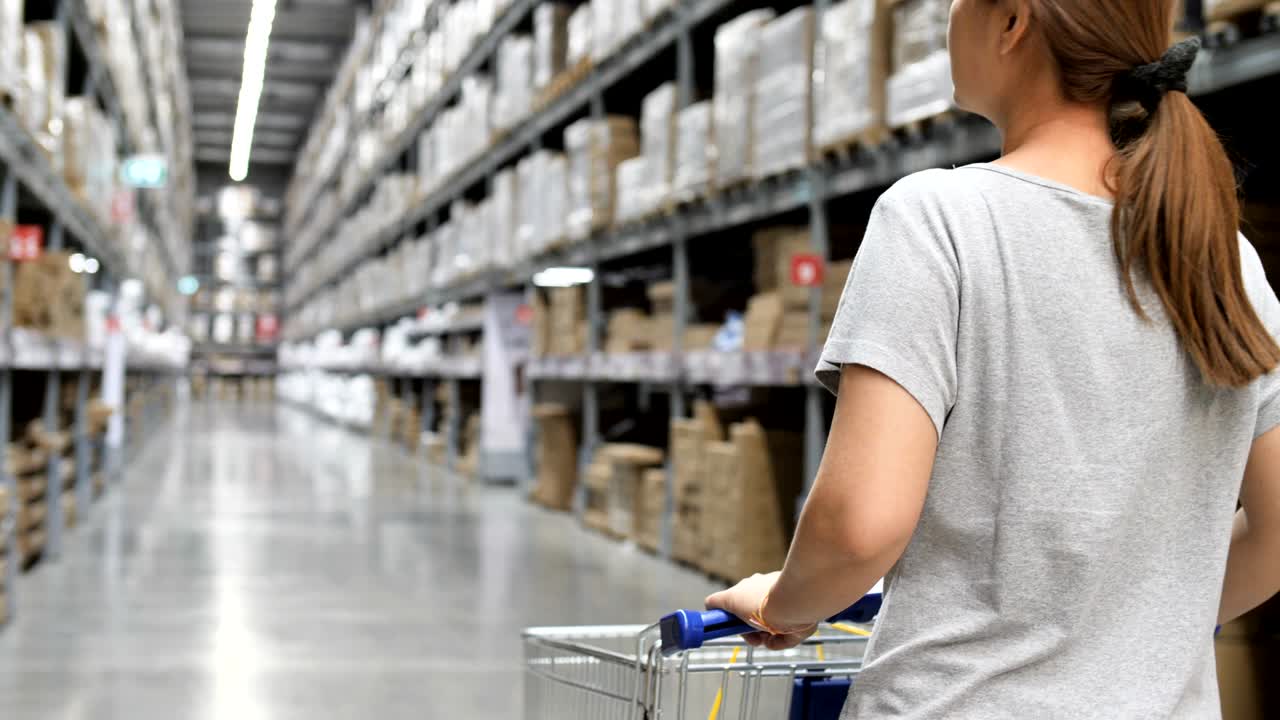 mujer asiática en cámara lenta de 4k viaja en carrito de compras por el almacén, eligiendo muebles nuevos