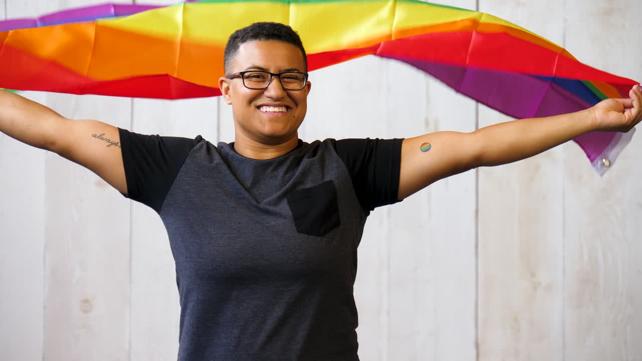 persona queer negra sosteniendo la bandera del orgullo gay ondeando sobre su cabeza
