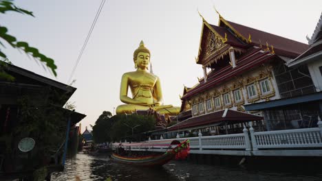 Nahaufnahme-Der-Prächtigen-Goldenen-Buddha-Statue,-Während-Ein-Langboot-Im-Ruhigen-Fluss-Vorbeifährt