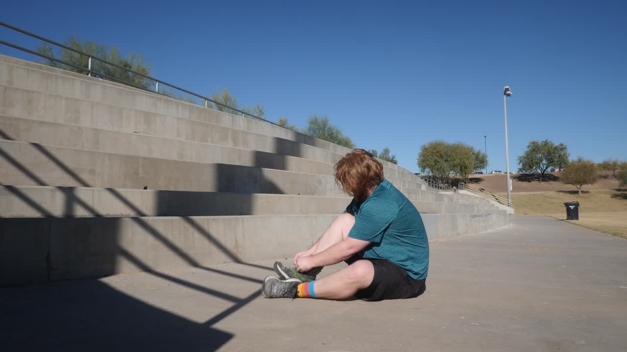 Overweight red haired man sits during workout from pain in his foot.