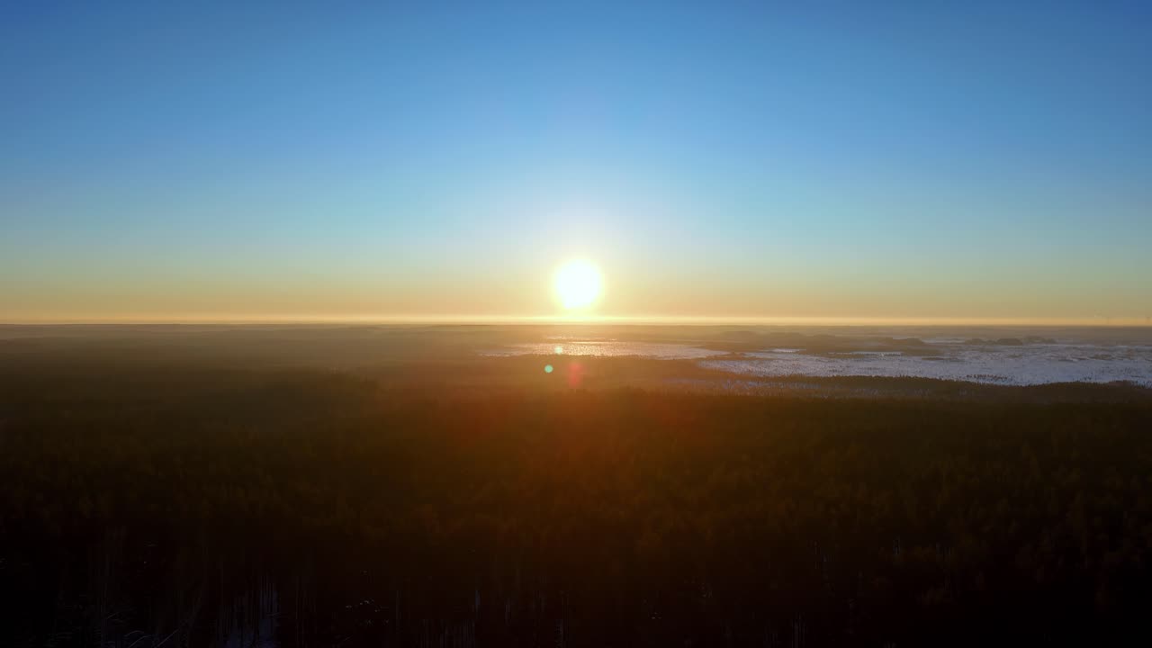 Breathtaking wide aerial panorama of a golden winter sunrise over a frozen northern landscape with dense dark evergreen forests and snow covered plains under a clear vibrant blue and orange sky
