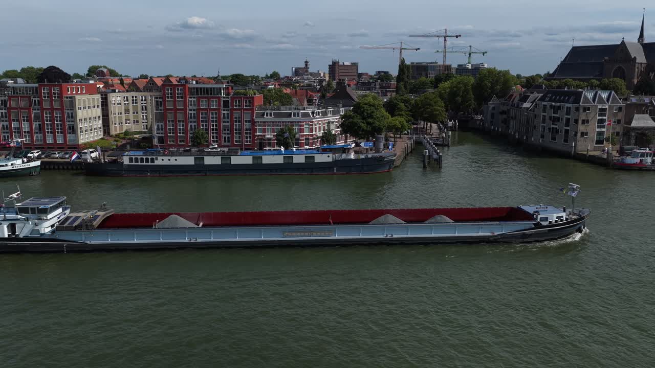 Cargo ship moves along river with city and historic buildings in view