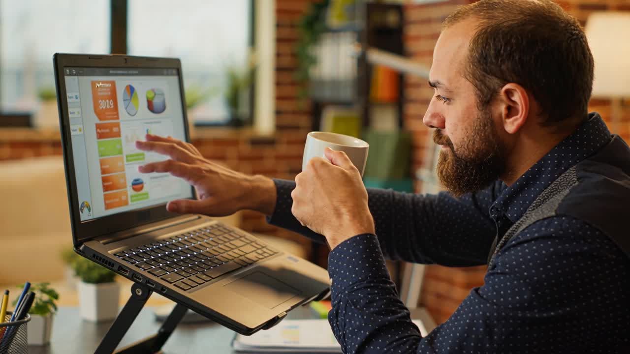 Glancing at dashboard blue-shirt man with mug tapping laptop typing reviewing at office, copy space