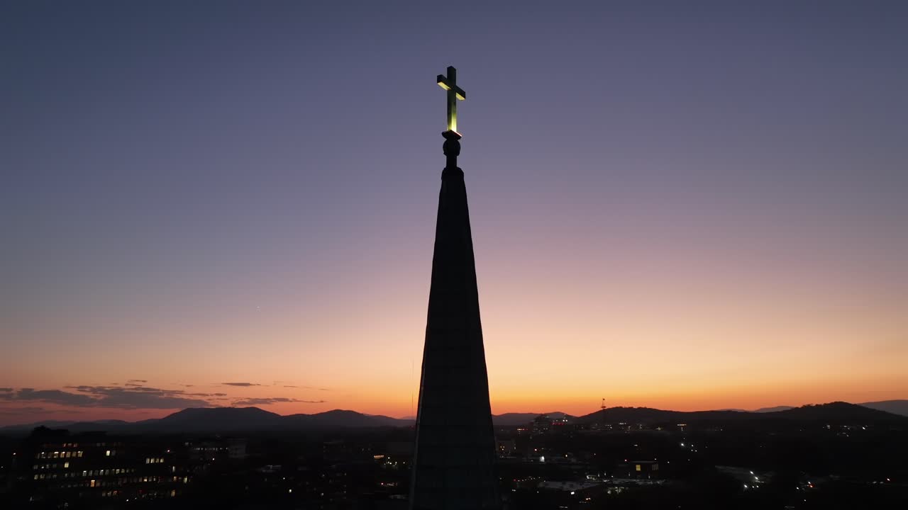 Aerial shot of cross on top of church tower at dusk. Sunset time with moon at night sky. small american town in Virginia. Orbit shot of silhouette.