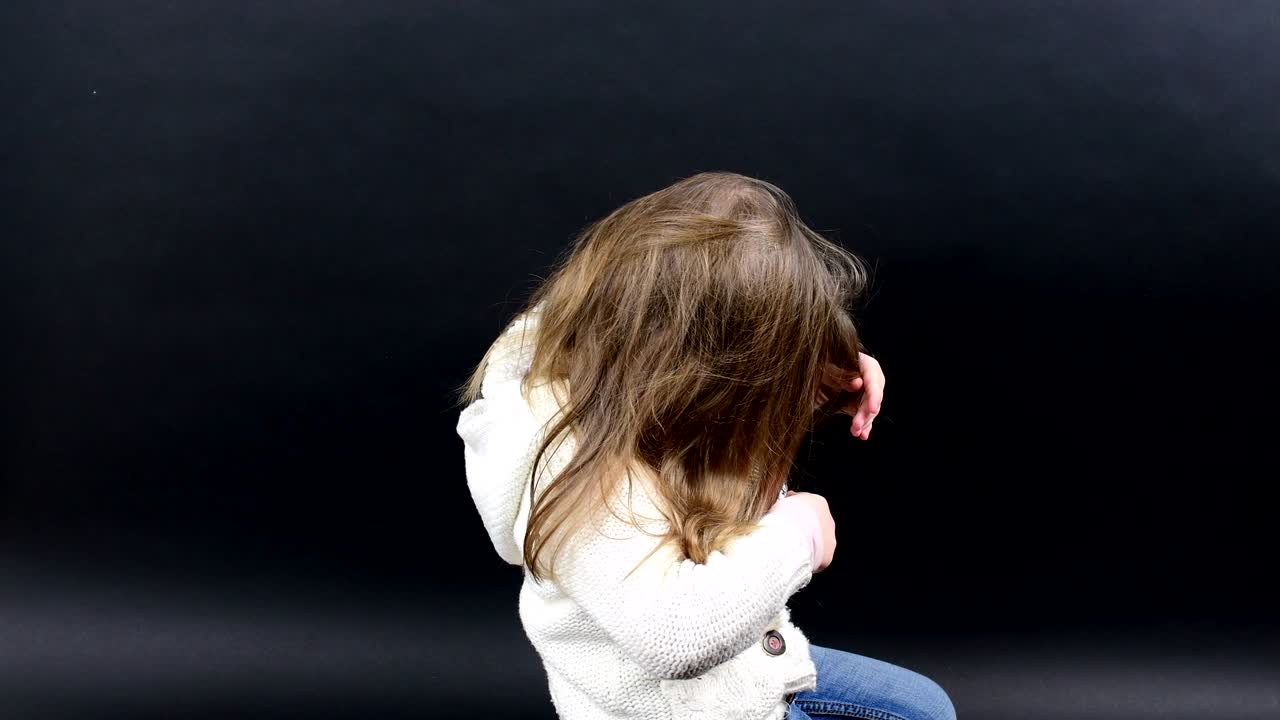una niña linda se peina el cabello. una niña pequeña está vestida con ropa de invierno. una niñita linda con fondo negro.