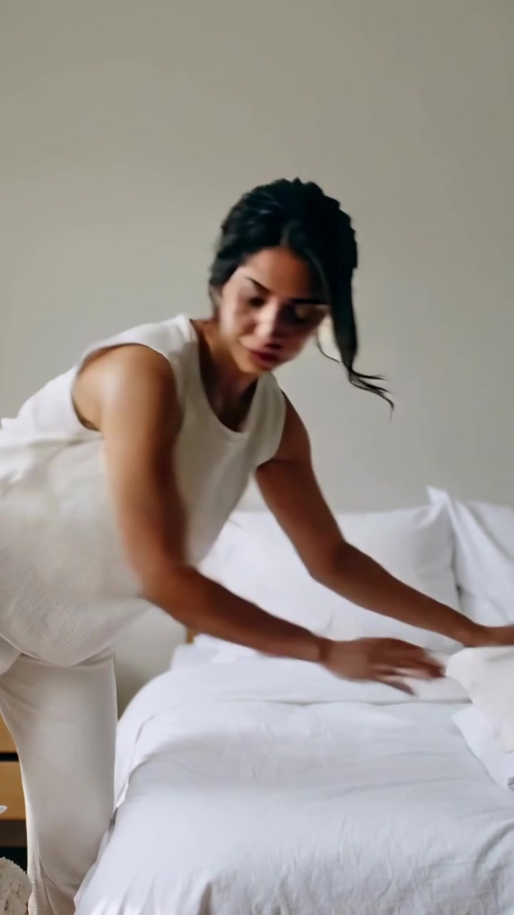Video verticale: Donna in top che tiene il cuscino a sinistra, sistema e liscia il letto per allinearlo, spazio per il testo.