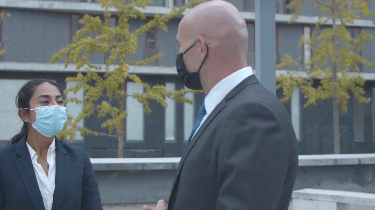 счастливые коллеги по бизнесу в масках на лицах встречаются в офисном здании, приветствуют друг друга ударами локтей и разговаривают