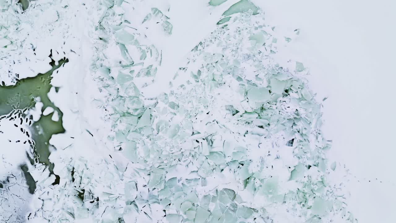 Vista aerea con drone di creste frastagliate di ghiaccio marino e lastre rotte vicino a una costa rocciosa invernale, con sacche di acqua di scioglimento color turchese e disegni modellati dal vento.