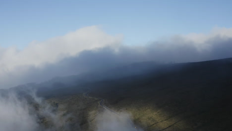 Winding-road-over-the-Haleakala-volcano-at-daylight,-while-clouds-moving-over-the-mountain-side-on-Maui,-Hawaii