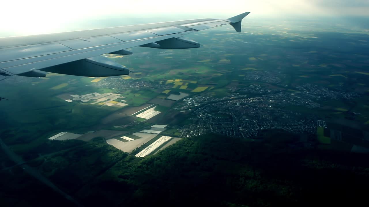 Flyvinge over grønne jorder og en fjern by