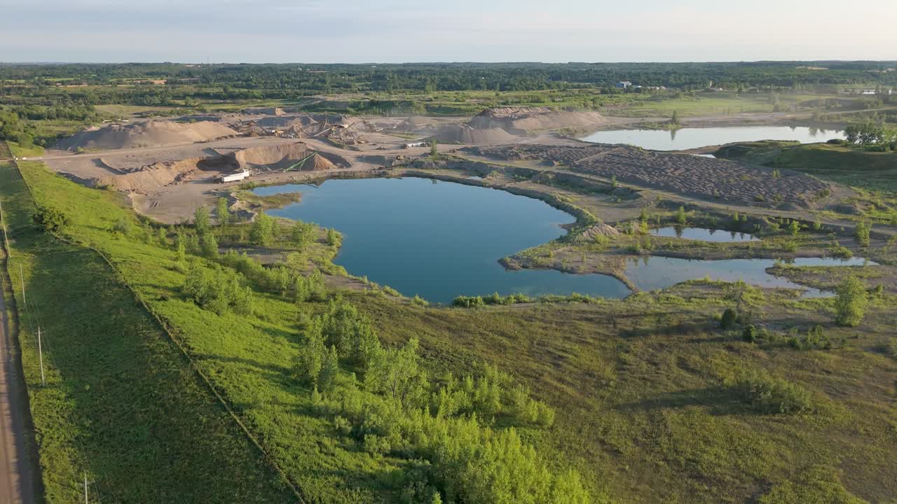 Aerial view of a vast gravel pit with lakes and greenery, serene landscape