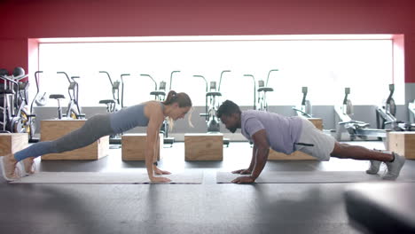 joven mujer blanca en forma y hombre afroamericano realizan tablas en el gimnasio