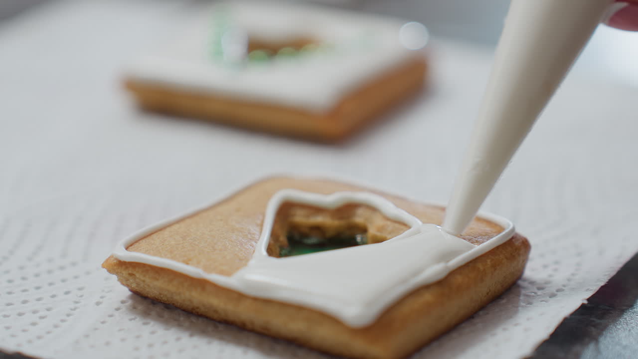 텍스처 된 종이에 놓인 쿠키에 대한 아이싱 프로세스의 클로즈업, 배경에 다른 장식 된 쿠키와 함께, 하 글래싱이 녹색 채우기를 둘러싸고 파이프됩니다.