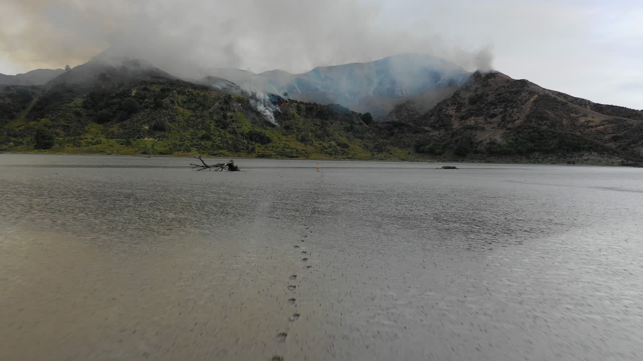 vista aérea de una mujer caminando a través de una llanura de barro hacia el humo de un incendio forestal