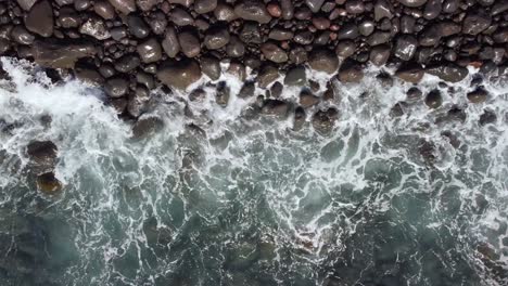 water-waves-splashing-into-pebble-rocks-at-the-seashore-in-Canary-Island,-Tenerife,-static