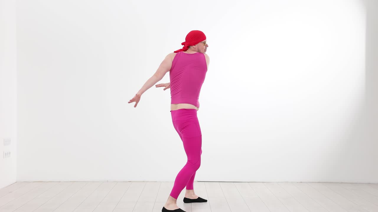 Mand i et farverigt pink outfit danser og poserer i et hvidt studie