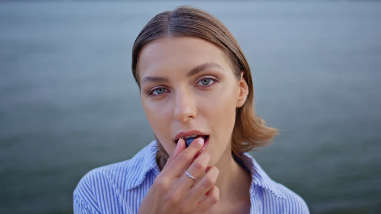 Woman eating blueberries standing by sea windy weather closeup. Portrait lady