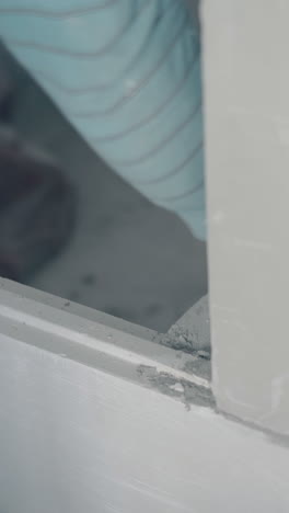 professional painter removes dry grey glue from large gypsum plasterboard construction close view