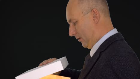 adult caucasian man in classical formal suit get present open gift box. man looking into gift box and spot light at his face. close up head shot. alpha channel chroma key transparent. side view.