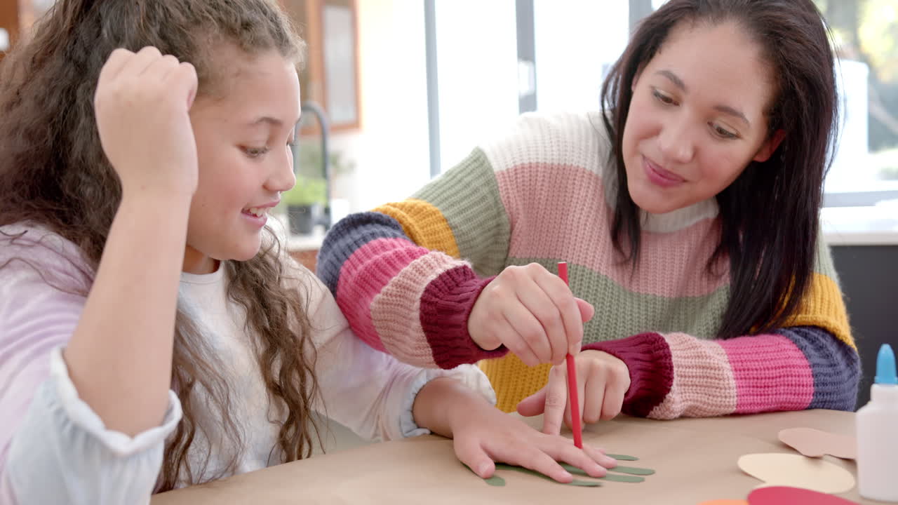 madre y hija bi-raciales felices jugando con papel de colores y sonriendo en la sala de estar soleada