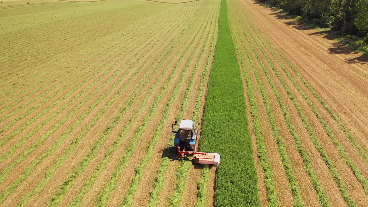Aerial view of tractor in the field in summer. Special technology for mowing green grass in process on the field background in sunny day.