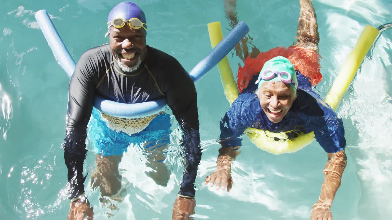 Video of happy senior african american couple swimming in pool