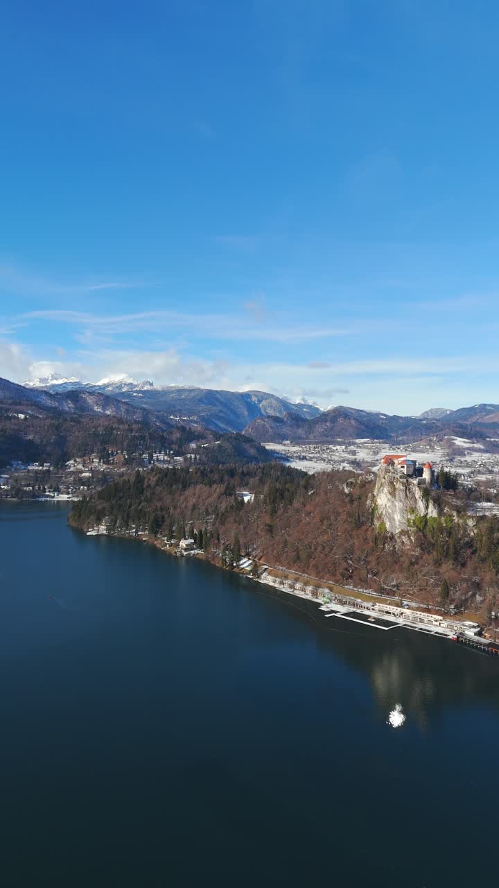 Ripresa verticale con drone che mostra il medievale Castello di Bled arroccato su una scogliera sopra il Lago di Bled in Slovenia durante l'inverno. Filmato di alta qualità 9:16 per contenuti di viaggio, turismo e inverno europeo