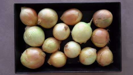 overhead shot of uncooked and unpeeled whole white onions in a container