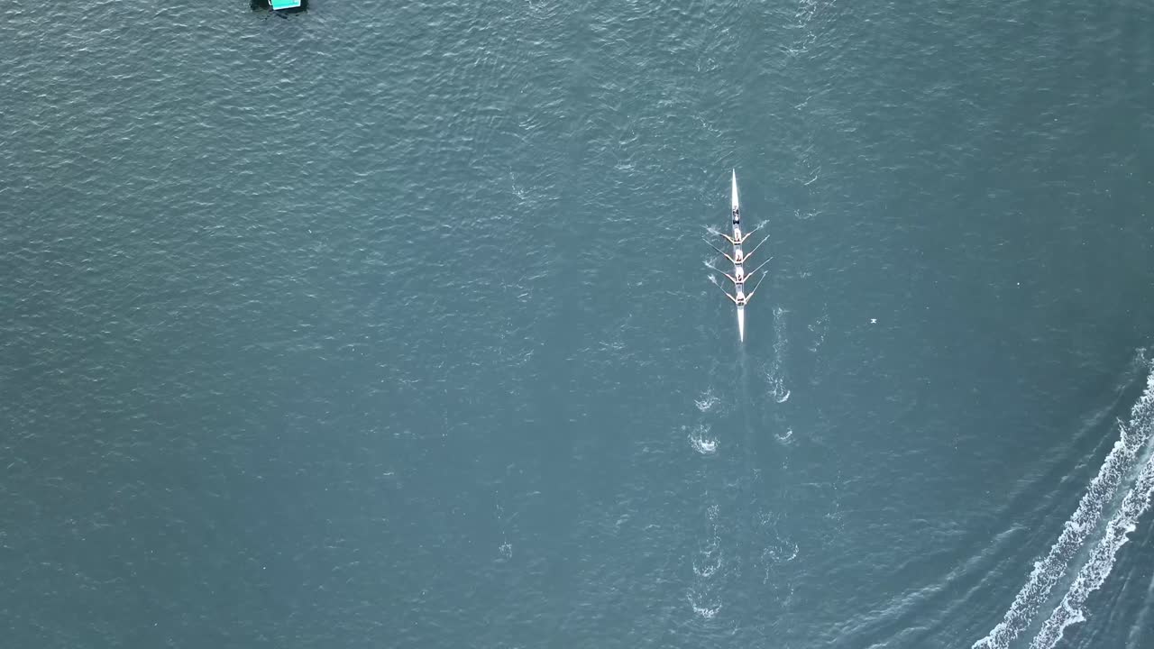 Tracking Aerial shot of rowers rowing down a river past boats.