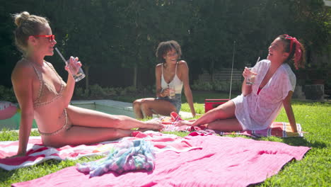 diverse female friends relaxing by pool, enjoying sunny day with drinks and laughter
