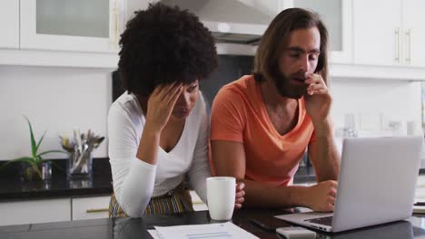 stressed mixed race couple using laptop and calculating finances in the kitchen at home