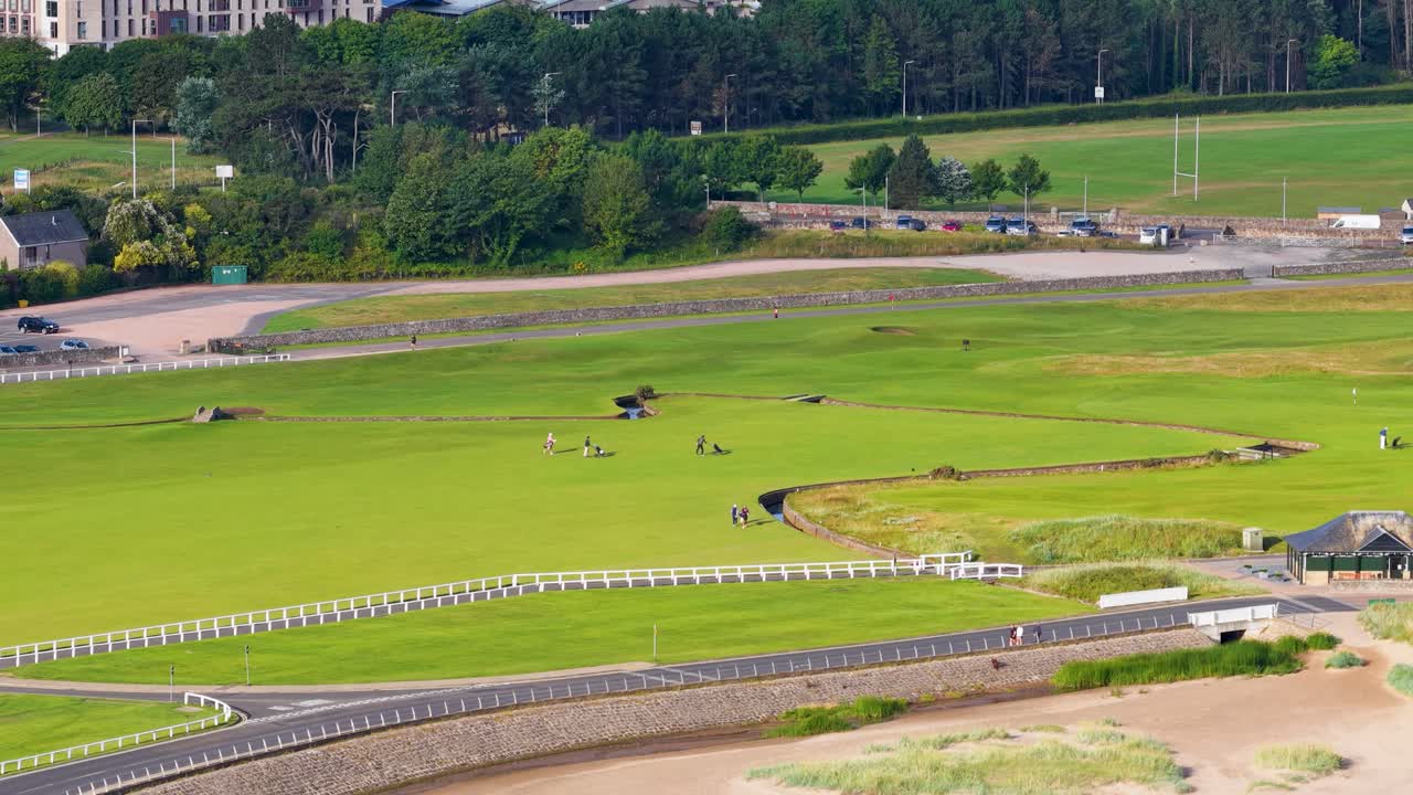 Drone captures golfers playing on lush green fairway, bright daylight, wide shot, St Andrews
