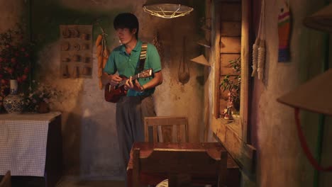 young asian male playing a ukulele while walking around a rustic room