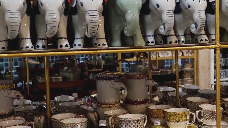 A collection of elephant figurines and intricately designed ceramic cups made in Thailand.