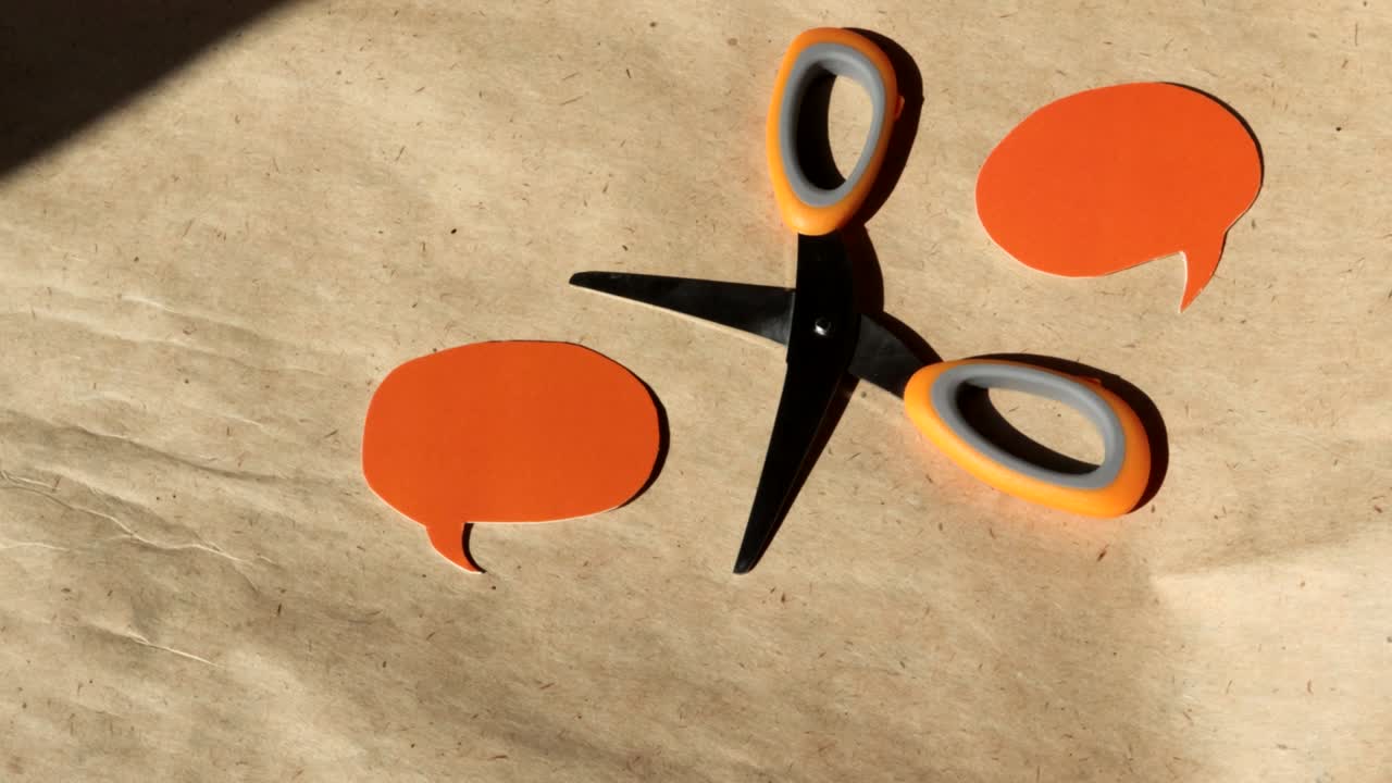 4k video, close-up of two speech bubbles cut out of orange paper and open scissors, DIY concept. Turn on brown kraft paper, top view