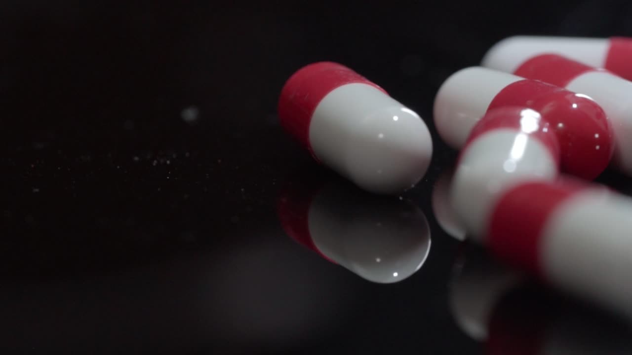 Pan right shot of red and white medicine capsules on reflective black surface, studio lighting
