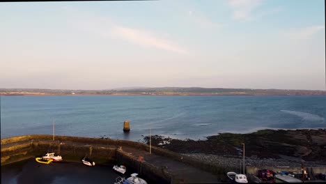 Liscannor-Co-Clare-drone-footage-showing-fishing-boats-in-the-harbour-at-low-tide-in-the-evening-sunshine,-on-the-main-road-to-the-Cliffs-of-Mohor,-with-Lahinch-town-in-the-distance-looking-east