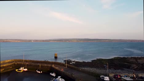 imágenes de drones de liscannor co clare que muestran barcos de pesca en el puerto durante la marea baja bajo el sol de la tarde, en la carretera principal a los acantilados de mohor, con la ciudad de lahinch en la distancia mirando hacia el este