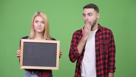 young couple holding blackboard and looking shocked together