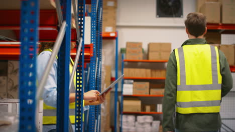 female team leader with digital tablet in warehouse training male intern standing by shelves