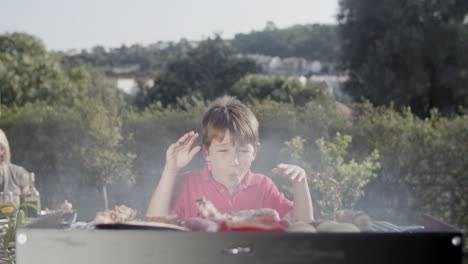 funny preteen boy waving hands and blowing at barbecue grill