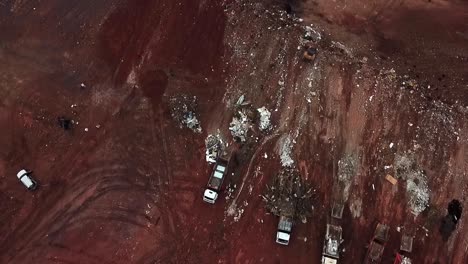 Dump-trucks-unloading-piles-of-trash-in-a-huge-landfill---aerial-view