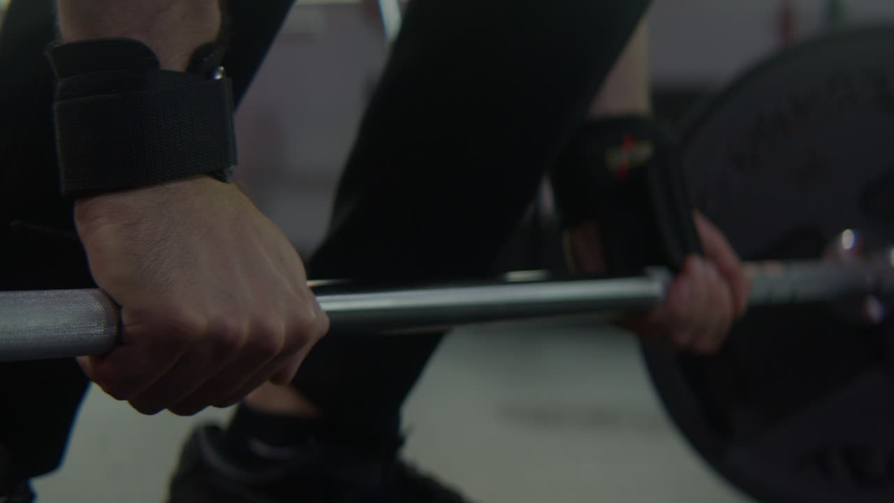 an athlete wrapping straps around barbell getting ready for deadlifting, close up shot
