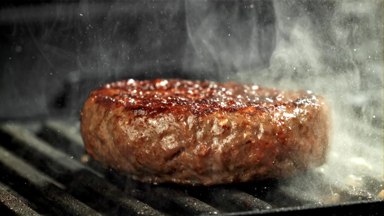 Nærbillede af en lækker burgerbøf, der griller med røg