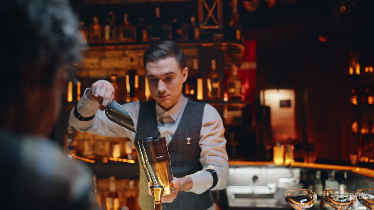 Ung bartender tilsetter is i shaker ved bardisken, nærbilde. Profesjonell mann