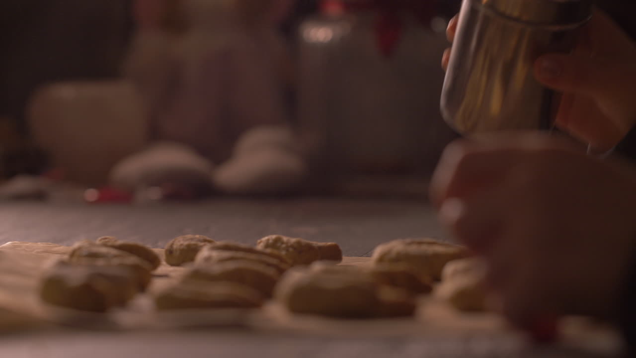 Little child's hands sprinkling flour over raw cookies on baking sheet. Close up